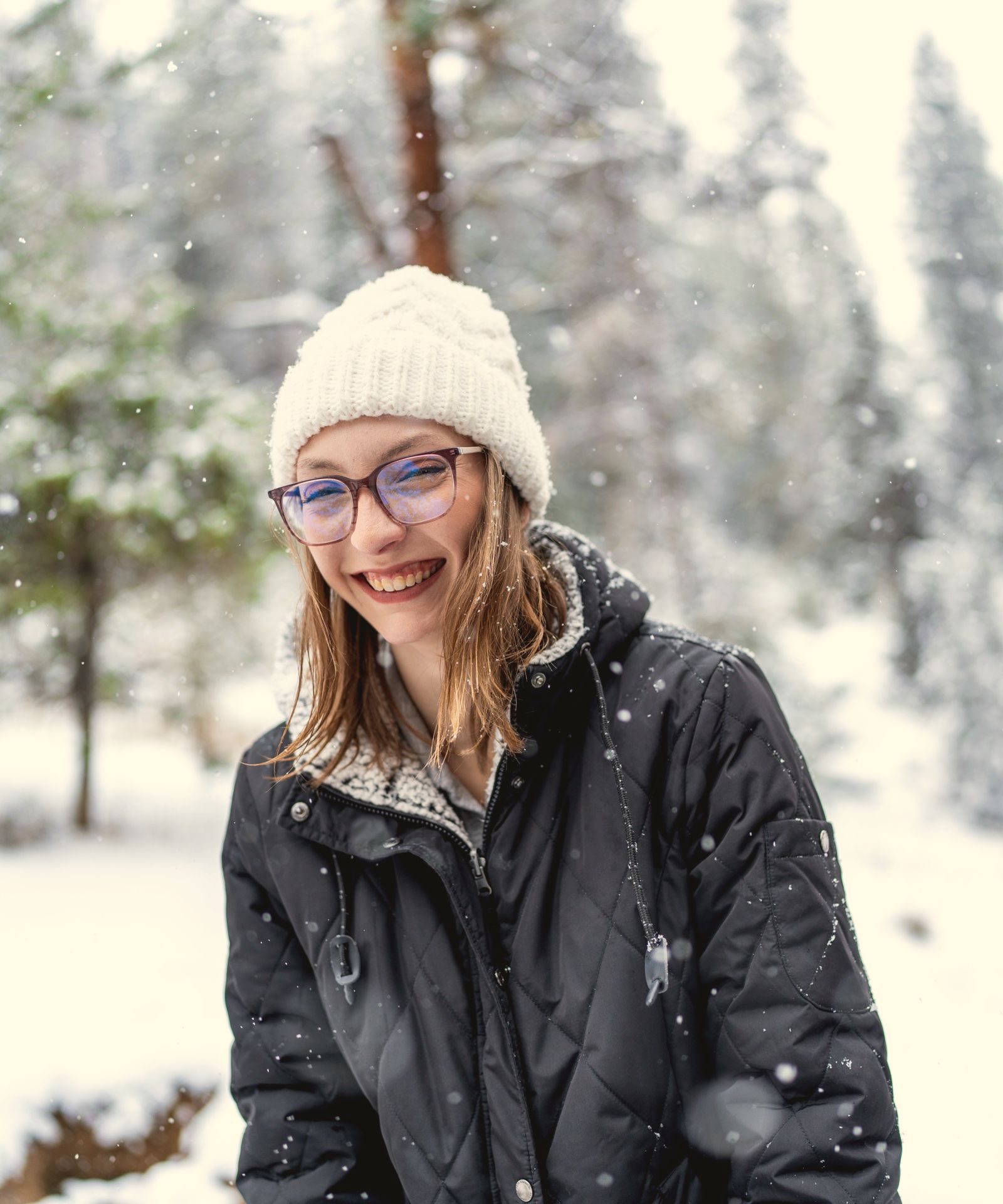 Stephanie in a cream knit hat, smiling as snow falls